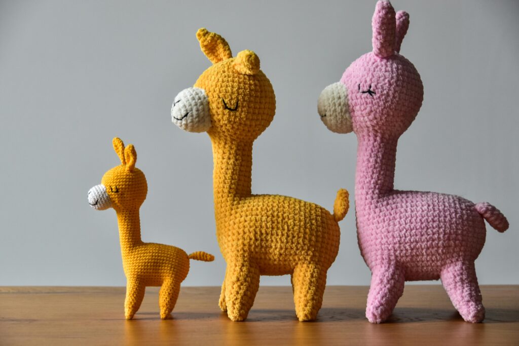 Three adorable crocheted llama toys in vibrant colors on a wooden table.